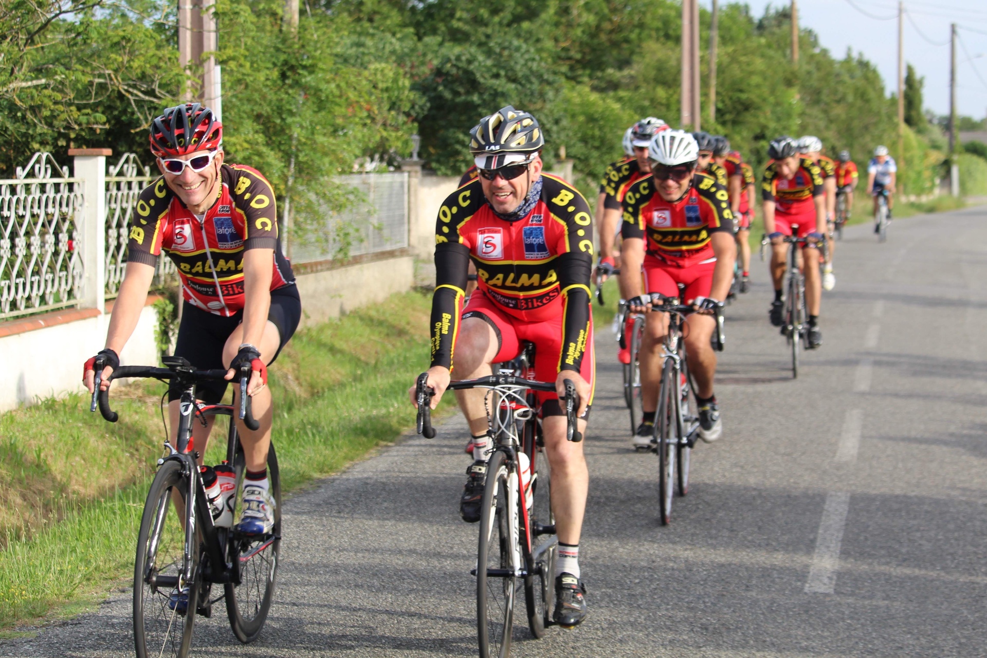 Cyclistes du BOC souriants roulant côte à côte sur une petite route de campagne