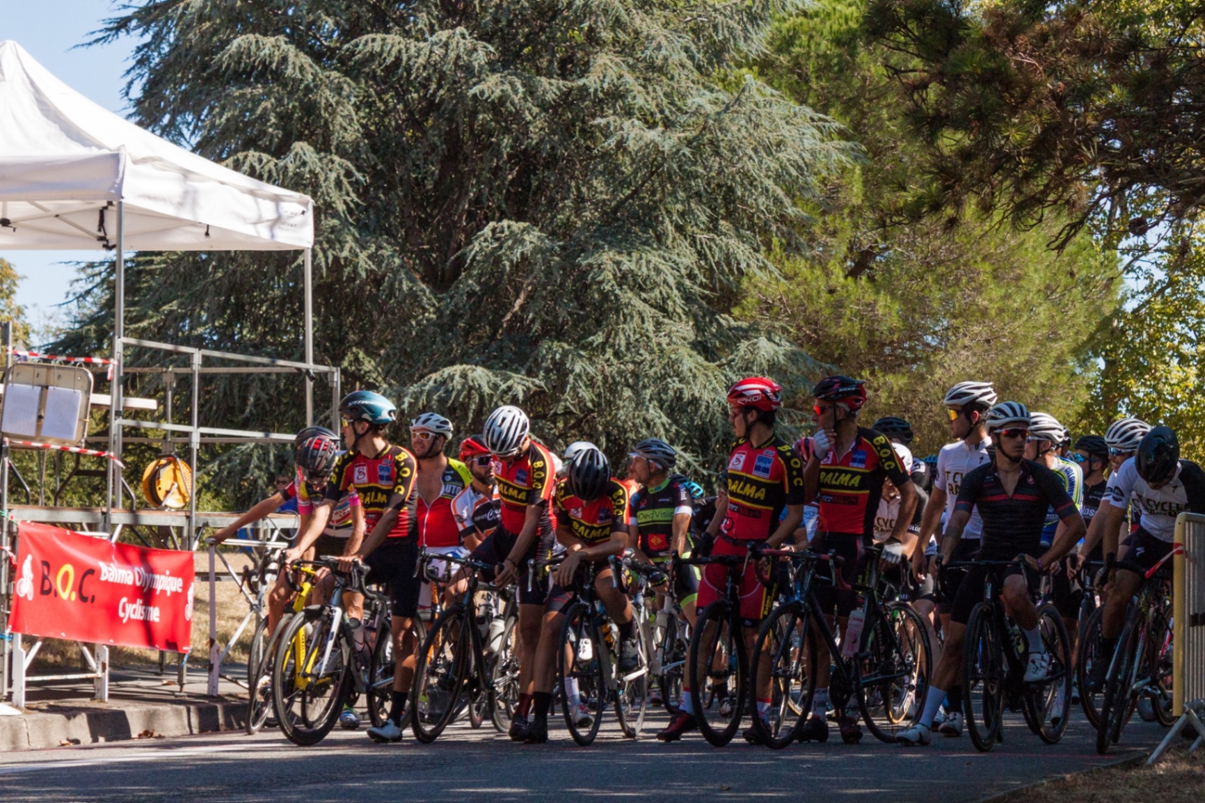 Peloton aligné au départ d'une course devant la banderole Balma Olympique Cyclisme